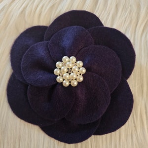 May include: A dark purple felt flower with a pearl and rhinestone embellishment in the center.