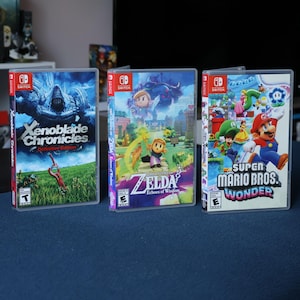 May include: Three Nintendo Switch game cartridges: Xenoblade Chronicles Definitive Edition, The Legend of Zelda: Echoes of Wisdom, and Super Mario Bros. Wonder. The cartridges are arranged from left to right.