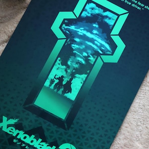 Può includere: Un poster per il videogioco Xenoblade 2, con una combinazione di colori verde acqua e blu scuro. Il poster presenta una citazione e il logo del gioco. Due statuette sono posizionate vicino al poster.