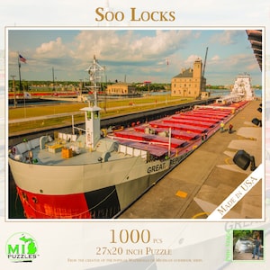 May include: A 1000 piece jigsaw puzzle featuring a red, white, and black freighter ship passing through the Soo Locks in Sault Ste. Marie, Michigan. The ship is labeled "Great Republic" and the puzzle is labeled "Soo Locks".