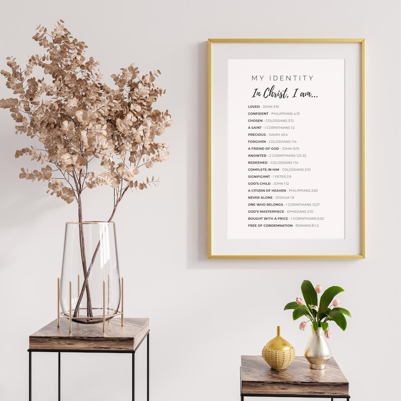 May include: A framed print with gold trim displays the text "MY IDENTITY In Christ, I am..." with a list of affirmations. The print is displayed on a white wall, next to a vase with dried flowers and a small table.