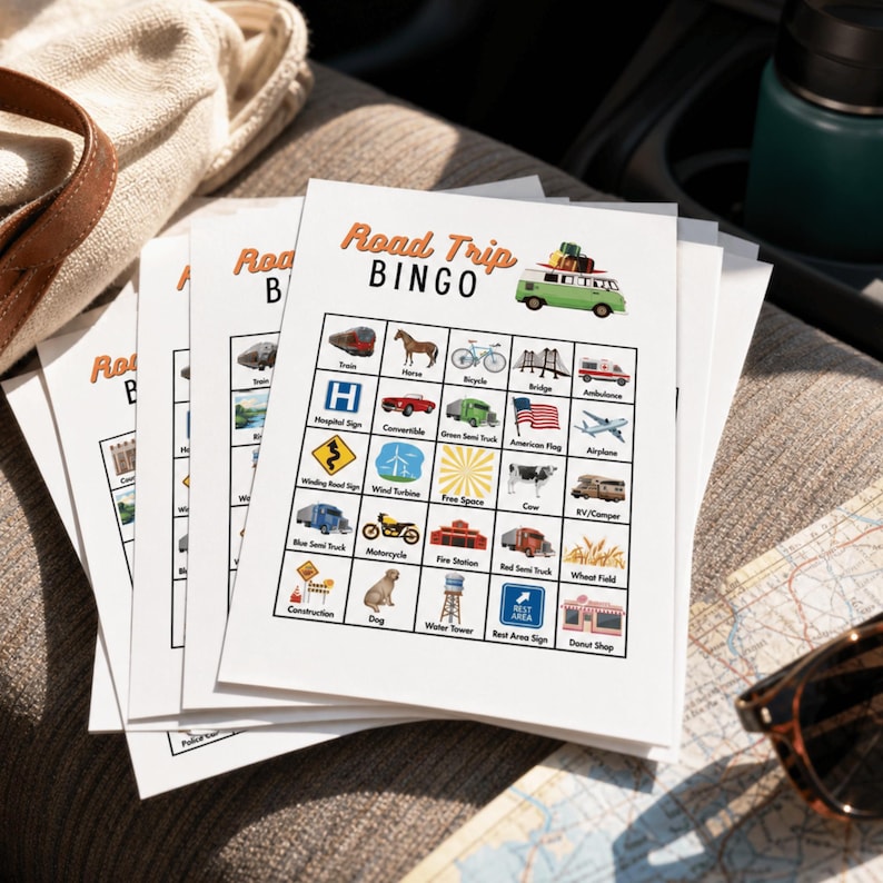 May include: A stack of white paper Road Trip Bingo game cards featuring a green camper van illustration at the top. Each card contains a five-by-five grid of colorful icons representing various items to spot, including a train, horse, bicycle, bridge, ambulance, and American flag.