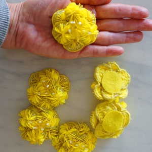 May include: Five yellow fabric flower embellishments with a variety of textures. Some are made of layered fabric petals, while others have a more rounded, smooth texture.