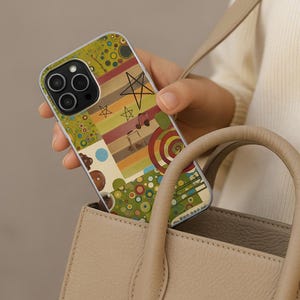 May include: A colorful phone case with a unique design featuring stars, musical notes, and geometric shapes in shades of green, brown, and orange. The case is held in a beige handbag.