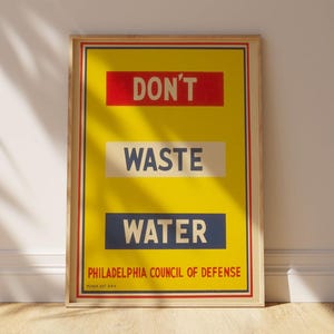 Può includere: Un poster vintage incorniciato con sfondo giallo e la scritta "DON'T WASTE WATER". Il poster include il testo "PHILADELPHIA COUNCIL OF DEFENSE" ed è incorniciato in una cornice di legno chiaro.