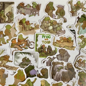 May include: A collection of colorful stickers featuring illustrations of frogs and toads. The stickers are in various poses and settings, including riding bikes, sitting on logs, and fishing. The stickers are perfect for adding a touch of whimsy to journals, laptops, and other surfaces.
