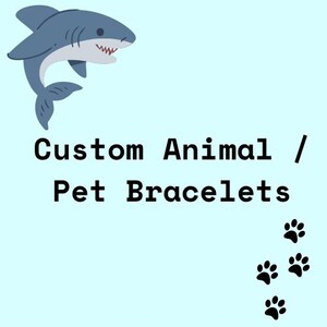 May include: An illustration of a blue shark against a white background. The text "Custom Animal / Pet Bracelets" is below the shark. There are four black paw prints in the bottom right corner of the image.