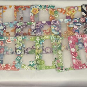 May include: A set of 12 colorful plastic picture frames with various designs and patterns. The frames are decorated with stickers, glitter, and other embellishments. The frames are all different sizes and shapes.