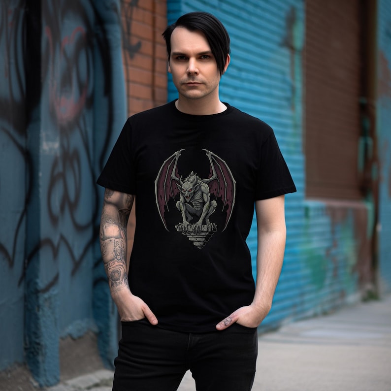 May include: Black t-shirt featuring a detailed illustration of a gargoyle with outstretched wings. The gargoyle is depicted in shades of gray and red, perched atop a stone structure. The shirt is a classic crew neck style.