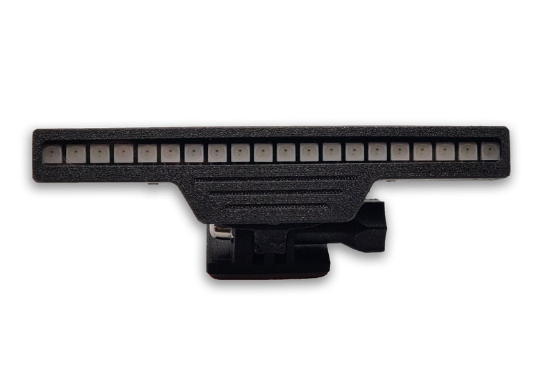 May include: A black light bar with a row of white LED lights. The light bar has a mount on the bottom for attaching to a surface.