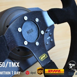 Op de afbeelding: Zwart racestuur met een zwarte suède grip en een zwart metalen frame. Het stuur heeft de tekst "KSS" en "OMP" erop. De tekst "FOR T150/TMX" is ook zichtbaar.