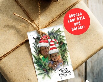 May include: A Christmas gift tag featuring two children wearing Santa hats, framed by a watercolor wreath of pine needles and pine cones. The tag reads "Merry Christmas" in script. A red circle with the text "Choose your hats and border!" is also visible.