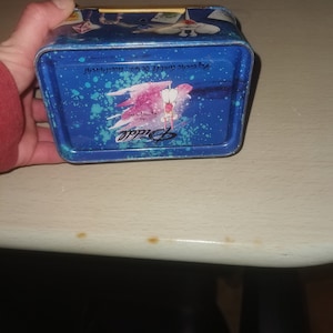 May include: Blue metal tin with a pink and white butterfly design and the text "Diddle" and "www.diddle.com.au".