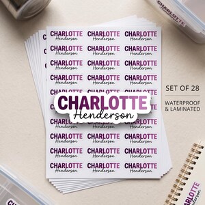 May include: A set of 28 waterproof and laminated rectangular stickers featuring the name Charlotte Henderson in a purple gradient font. The stickers are displayed on a sheet, with individual labels applied to a metal bottle and plastic containers.