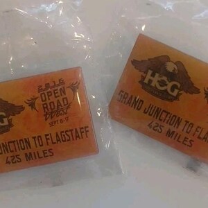 May include: Two rectangular orange pins in clear plastic packaging. Each pin features an eagle graphic, the text HOG, 2016 OPEN ROAD WEST SEPT 8-17, and GRAND JUNCTION TO FLAGSTAFF 425 MILES. The design includes dark brown lettering and eagle imagery.