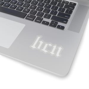 Könnte beinhalten: Ein weißer Vinyl-Aufkleber mit dem Wort "hen" in gotischer Schriftart, platziert auf einem silbernen Laptop.