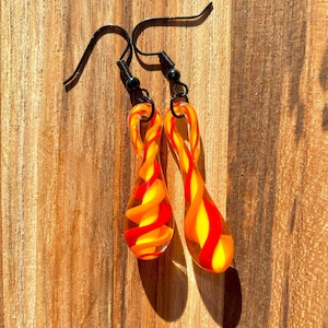 May include: A pair of dangle earrings with red and yellow glass drops. The drops are twisted and have a swirl pattern.
