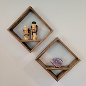May include: Two diamond-shaped wooden shelves mounted on a wall. The top shelf has two wooden figurines, and the bottom shelf has a large amethyst crystal.