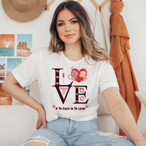 May include: White t-shirt with a black graphic of the word "LOVE" with medical symbols and a red heart. The text below the graphic says "# To Care Is To Love".