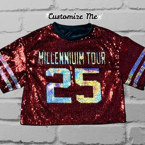 May include: A red sequined crop top with a white and iridescent sequined number "25" and the text "Millennium Tour" in white sequins.