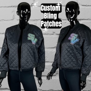May include: Two black quilted jackets with a large iridescent rhinestone patch on the left chest. The patch says "SV". The jackets are on mannequins against a white brick wall. The text "Custom Bling Patches" is in the top center of the image.