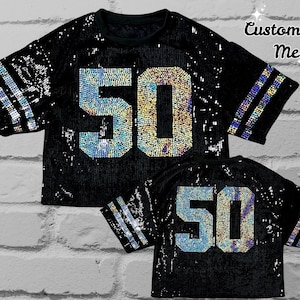 May include: Black sequined jersey with the number "50" in iridescent sequins on the front and back. The sleeves have iridescent stripes. The text "Customize Me" is in the upper right corner.