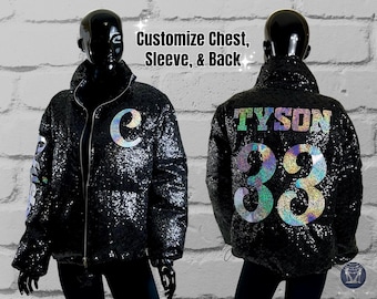 May include: Black sequin puffer jacket with iridescent details. The jacket features a zipper closure, a stand-up collar, and a large letter "C" on the chest. The back of the jacket has the text "TYSON" and the number "93" in iridescent sequins.