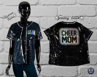 May include: Black sequined cheer mom jersey with a rainbow glitter design. The back of the jersey says "Cheer Mom" and the front has a space for a custom name.
