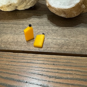May include: Two small yellow plastic containers with black lids. The containers are on a wooden surface.