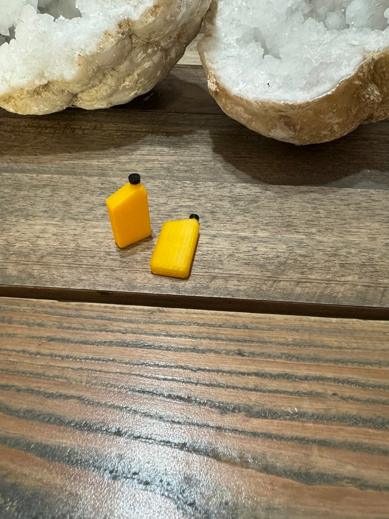 May include: Two small yellow plastic containers with black lids. The containers are on a wooden surface.