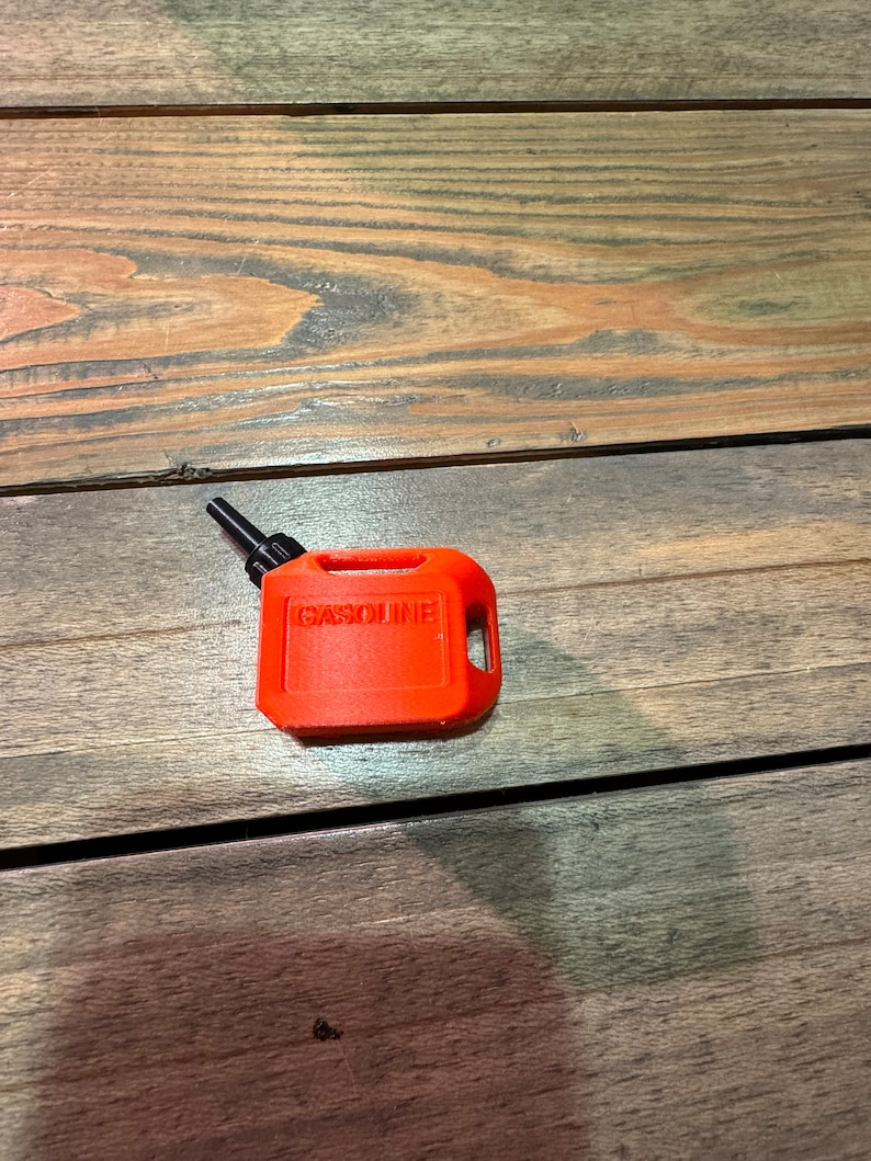 May include: A small, bright orange plastic gasoline can with a black spout and the word "GASOLINE" printed on the side.