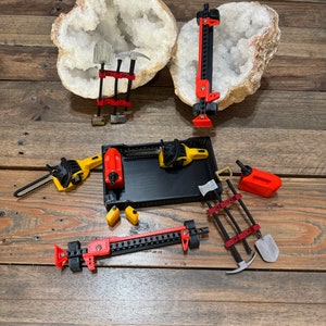 May include: A set of miniature tools, including a pickaxe, shovel, chainsaw, and jack, displayed on a wooden surface with two large white crystal formations.