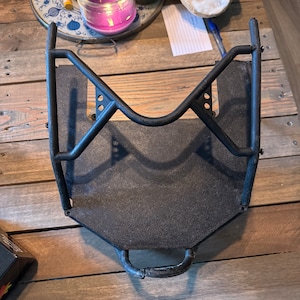 May include: Black metal frame with a flat, textured surface and a handle. The frame is designed to hold a small object, such as a phone or a tablet.