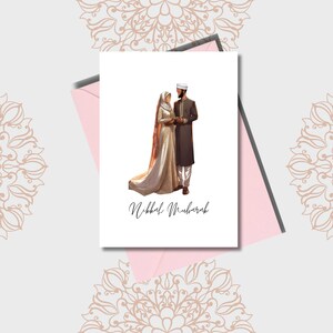 May include: A wedding card with a couple in traditional Islamic clothing. The card is white with a pink envelope and the text "Nikkah Mubarak" in black cursive.