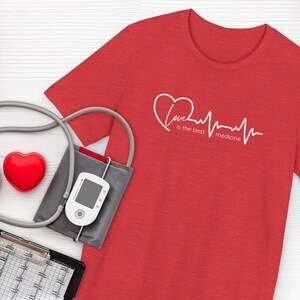 May include: A red t-shirt with the text "Love is the best medicine" in white, along with a heart and a heartbeat line. A red heart, a blood pressure monitor, and a stethoscope are also visible.