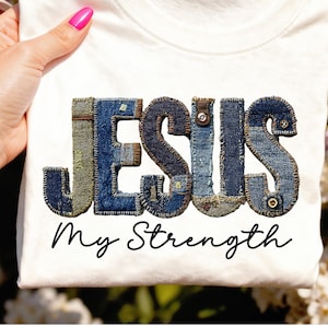 Könnte beinhalten: Weißes T-Shirt mit dem Wort "JESUS" in Jeans-Patchwork-Buchstaben und dem Schriftzug "My Strength" darunter. Die Jeansbuchstaben sind in Blau- und Grüntönen gehalten.