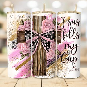Może przedstawiać: Zestaw trzech kubków ze stali nierdzewnej ze złotymi pokrywkami i słomkami. Kubki mają wzór krzyża z czarno-różową kokardą w kropki, różowymi różami i tekstem "Jesus fills my cup" z "psalm 23:5".