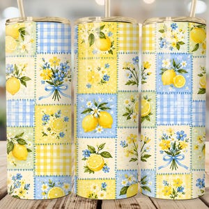May include: Three cylindrical tumblers featuring a patchwork pattern of yellow lemons, blue and yellow floral bouquets, and light blue and yellow gingham checks. Each tumbler includes a clear lid and a metal straw extending from the top.
