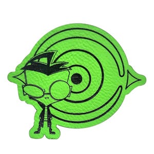 May include: A green cartoon character patch with black outlines. The character wears glasses and a black hat, set against a target-like design. The patch is likely made of leather or a similar material.