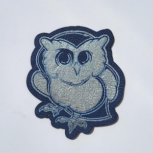 May include: A blue and silver glitter owl patch. The owl is cartoon-like with large eyes and a friendly expression.