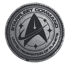 以下が含まれることがあります： 「STARFLEET COMMAND」と「UNITED FEDERATION OF PLANETS」の文字が円形に配置された銀色のパッチ。中央には、星と4つの小さな星をあしらった、様式化された矢印のエンブレムが描かれています。