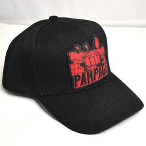 May include: Black baseball cap with a red and black "PAMPAGE" patch. The patch shows a red fist and a mechanical design. The cap is made of a durable fabric and has a curved peak.