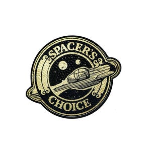 May include: A circular black and gold patch with the text "SPACER'S CHOICE" encircling a spaceship design. The spaceship is depicted in gold, with a trail behind it, set against a black background with two celestial bodies.