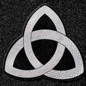 May include: A silver-colored triquetra patch featuring a textured, metallic finish. The design consists of three interconnected, pointed oval loops forming a continuous knot pattern, outlined with a thin black border against a black background.