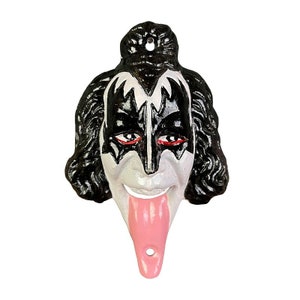 May include: Black and white cast iron bottle opener shaped like the face of a rock star with a long, pink tongue sticking out.
