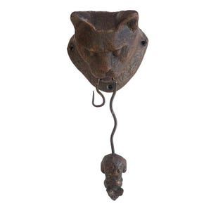May include: A cast iron wall hook in the shape of a cat's head with a mouse hanging from its mouth. The cat is brown and the mouse is gray.