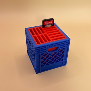 May include: A blue and red plastic crate with slots for storing Nintendo Switch game cartridges. A game cartridge is in one of the slots. The game cartridge is for the game Pokemon Legends: Arceus.
