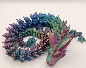 May include: A 3D printed articulated dragon figure featuring a multi-colored iridescent finish that shifts between shades of blue, green, and purple. The creature has a segmented body covered in sharp, crystal-like spikes along its back.
