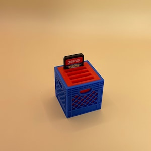 May include: A blue and red plastic crate with slots for storing Nintendo Switch game cartridges. A game cartridge is in the top slot. The game cartridge is for Pokemon Sword and Shield.