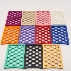 May include: A collection of twelve rectangular decorative panels in various colors, including purple, orange, green, black, and gold. Each panel features a honeycomb pattern, creating a visually appealing design. The panels are arranged on a white surface.